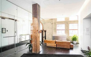 Un hall con un separador de vidrio, un banco de madera, una planta en maceta y una pared de ladrillo.