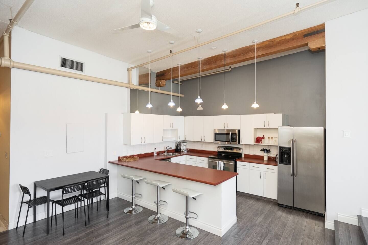 A modern kitchen with white cabinets, a central island, stainless steel appliances, and pendant lighting.