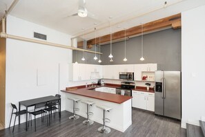 A modern kitchen with white cabinets, a central island, stainless steel appliances, and pendant lighting.