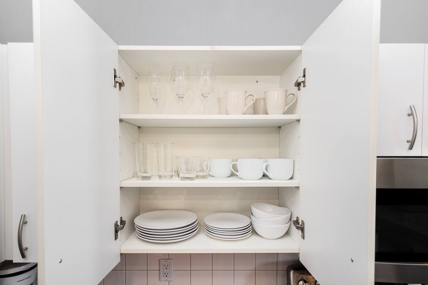 A kitchen pantry with white cabinets, shelves with glassware, cups, and stacked plates.