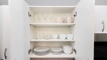 A kitchen pantry with white cabinets, shelves with glassware, cups, and stacked plates.