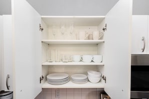 A kitchen pantry with white cabinets, shelves with glassware, cups, and stacked plates.