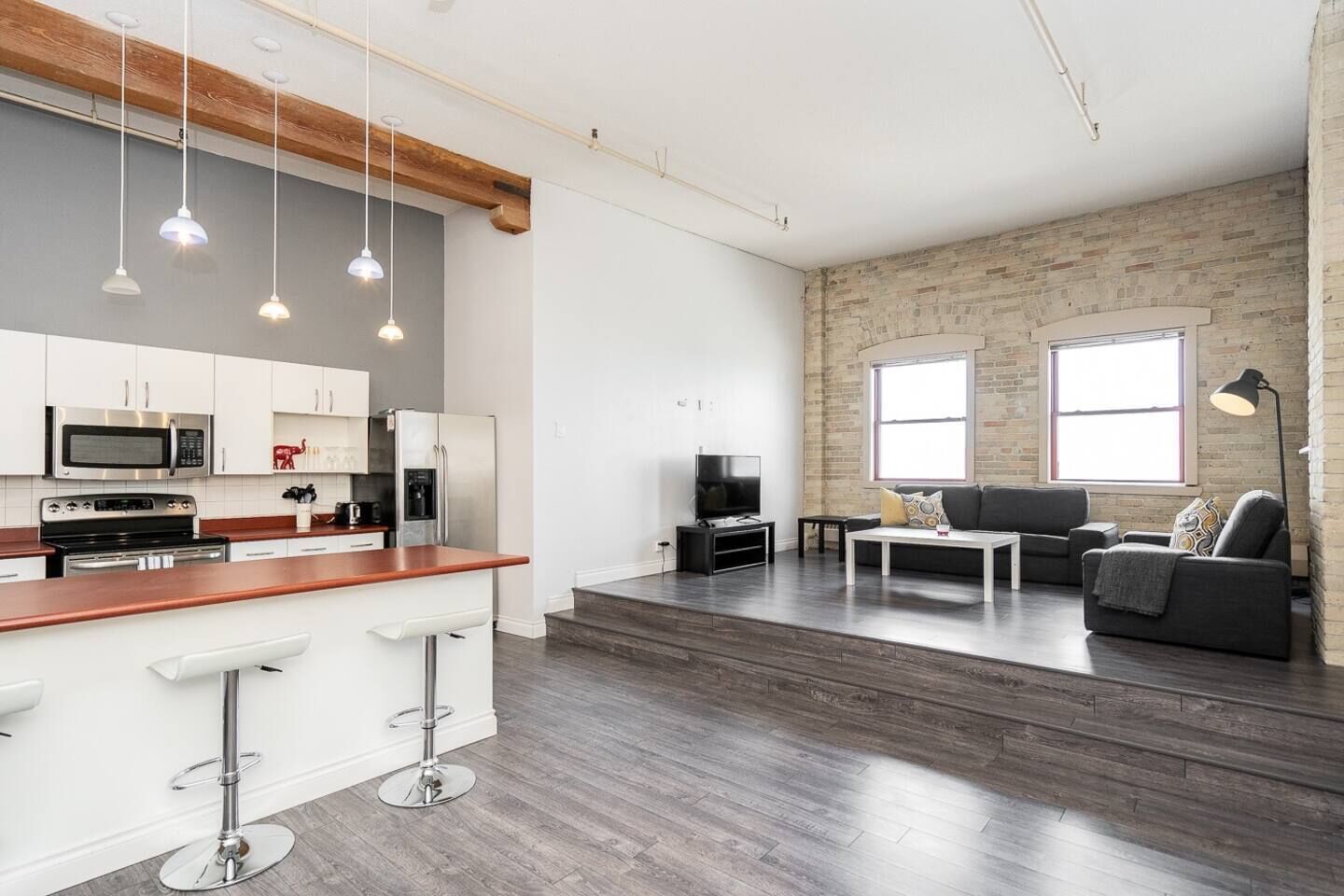A modern kitchen with white cabinets, stainless steel appliances, and a bar stool.