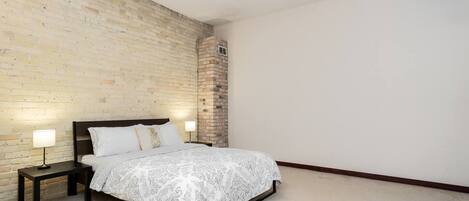 Un dormitorio con pared de ladrillo, una cama con colcha estampada, dos lámparas de noche y un pequeño pilar de ladrillo.