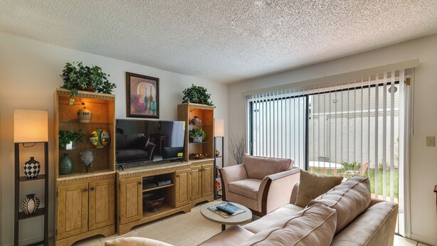 Ein Wohnzimmer mit Sofa, Fernseher, Holzschrank und einem Fenster mit Jalousien.
