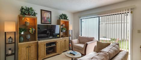A living room with a sofa, television, wooden cabinet, and a window with blinds.