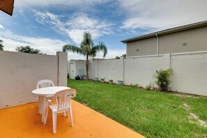 Eine Terrasse mit weißem Tisch und Stühlen, eine kleine Rasenfläche und ein Gebäude mit weißer Fassade.