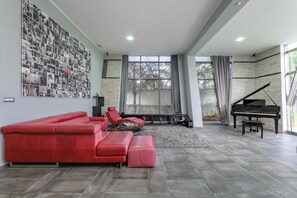 A modern living room with a red sectional sofa, a grand piano, and a large wall of black and white photographs.