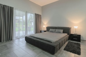 A modern bedroom with a large bed, two bedside tables, and a view through a window with curtains.