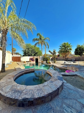 Una piscina con borde de piedra, rodeada de palmeras y un cielo azul despejado.