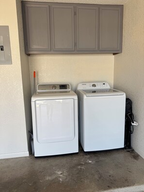 Two white front-loading washing machines in a laundry room with a grey cabinet above and a black bag hanging on the wall.
