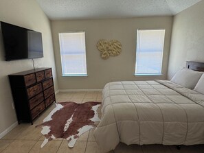 A bedroom with a bed, dresser, television, two windows with blinds, and a wall decoration. - Paradise Cove! Peaceful 3bedroom plus office home in friendly safe neighborhood! (Copperas Cove)