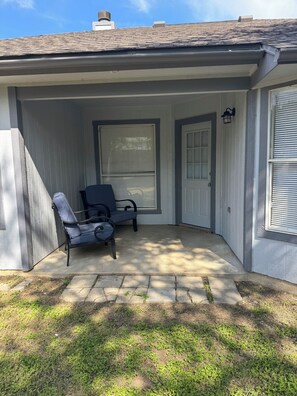 A covered patio area with a chair and a table, a door, and a window with shutters. - Paradise Cove! Peaceful 3bedroom plus office home in friendly safe neighborhood! (Copperas Cove)