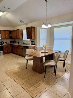 A modern kitchen with wooden cabinets, a dining table with chairs, and a large window with blinds. - Paradise Cove! Peaceful 3bedroom plus office home in friendly safe neighborhood! (Copperas Cove)