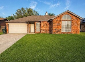 A single-story brick house with a garage, a large arched window, and a well-maintained lawn.