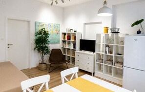 Ein modernes Wohnzimmer mit Fernseher, Bücherregal, Esstisch und Stühlen.