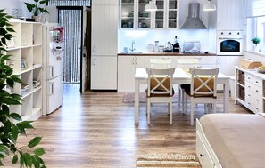 Une cuisine moderne avec des meubles blancs, un coin repas avec deux chaises et un plancher en bois.