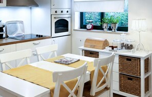 Eine moderne Küche mit weißen Schränken, einem eingebauten Backofen, einer Kaffeemaschine und einem Fenster mit Pflanzen.