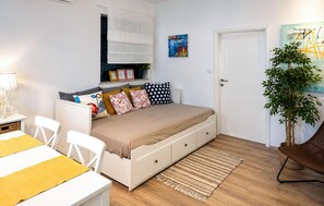 Ein Schlafzimmer mit einem Bett, Nachttischen, einem Schreibtisch, Stühlen, einer Pflanze und Bildern an den Wänden.