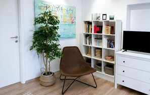 Ein Zimmer mit Bücherregal, Fernseher, Stuhl und einer Zimmerpflanze.