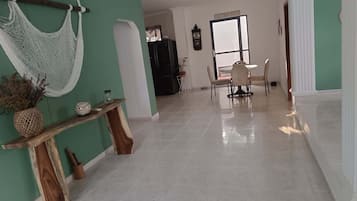 Un pasillo amplio con comedor, que incluye una mesa y sillas, una hamaca y una consola de madera con adornos.