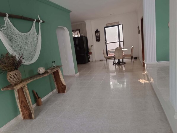 Un pasillo amplio con comedor, que incluye una mesa y sillas, una hamaca y una consola de madera con adornos.