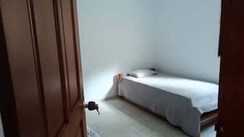 Pequeña habitación con una cama individual, puerta de madera y piso de baldosas.