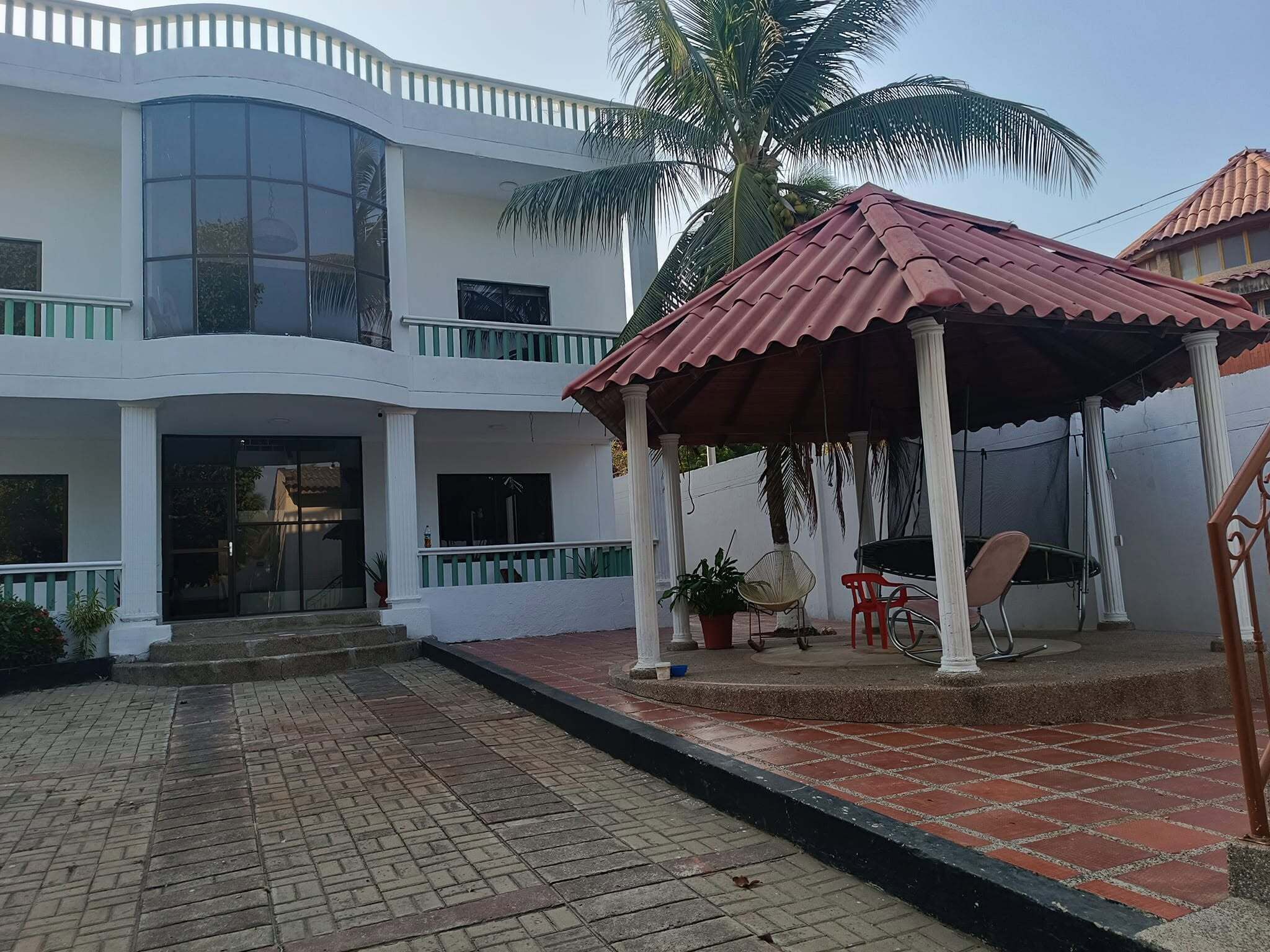 Un edificio de dos plantas con un patio techado, un ventanal grande y una palmera.