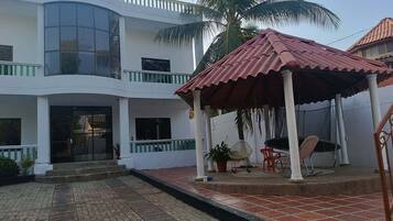 Un edificio de dos plantas con un patio techado, un ventanal grande y una palmera.