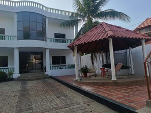 Un edificio de dos plantas con un patio techado, un ventanal grande y una palmera.