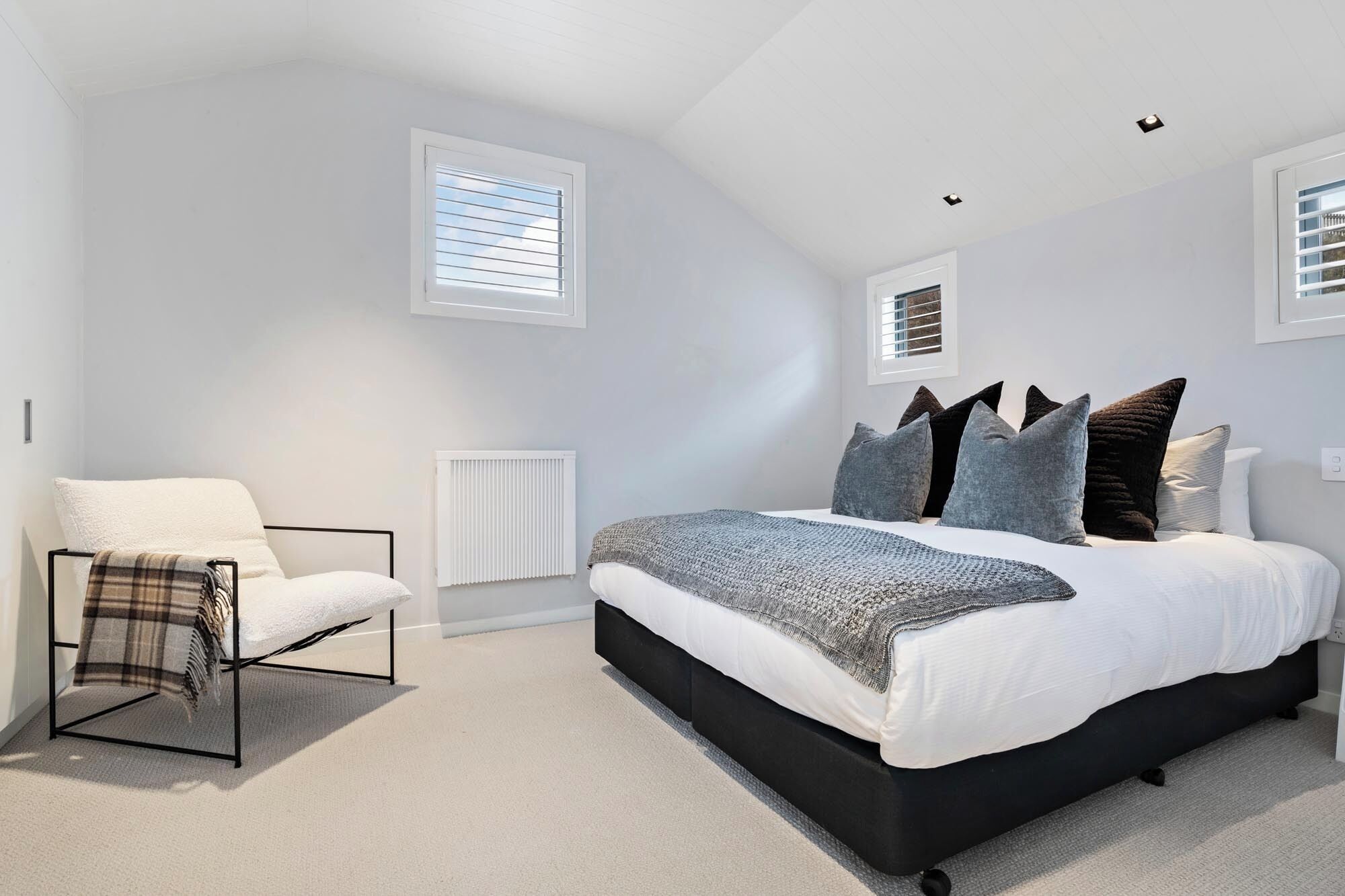 A bedroom with a bed, a chair, a radiator, and two windows.
