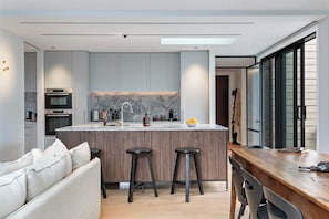 A modern kitchen with a central island, bar stools, and a wooden dining table. - Luxury Arrowtown Escape/Walk to Arrowtown Village (Arrowtown)