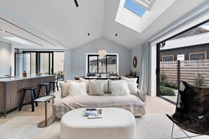 A modern interior with a central seating area, a kitchen with a bar, and a large window providing natural light. - Luxury Arrowtown Escape/Walk to Arrowtown Village (Arrowtown)