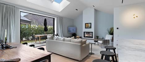 Ein modernes Wohnzimmer mit einer Couch, Fernseher, Kamin und einem Essbereich mit Tisch und Stühlen.