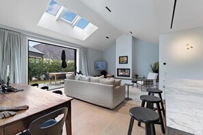Een moderne woonkamer met een bank, televisie, open haard en een eethoek met tafel en stoelen.