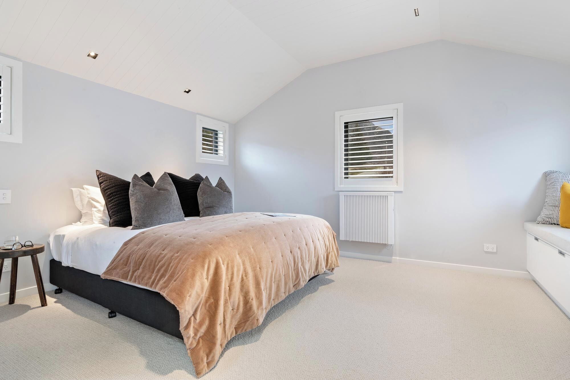A bedroom with a bed, bedside tables, a radiator, and windows with blinds.