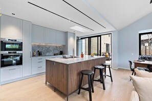 Une cuisine moderne dotée d’un îlot central, d’appareils électroménagers intégrés et d’une grande fenêtre.