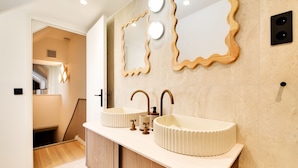 Un baño moderno con dos lavamanos, un mueble de madera y un diseño de espejo ondulado único.