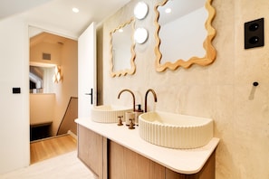Un baño moderno con dos lavamanos, un mueble de madera y un diseño de espejo ondulado único.