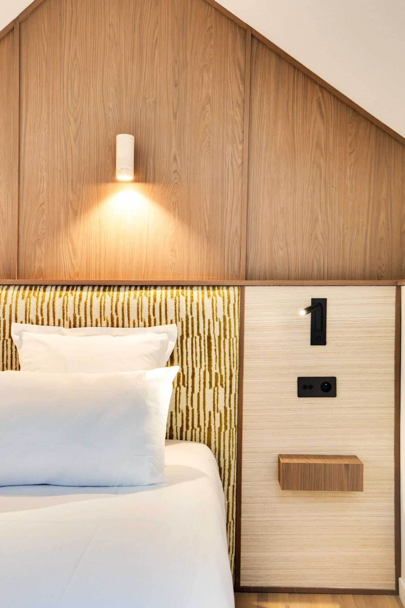 A bedroom with a wooden headboard, a bed with white bedding, and a nightstand with a lamp.