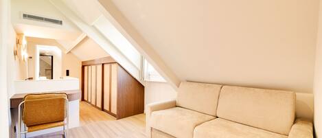 A modern loft bedroom with a sloped ceiling, a built-in desk, a cushioned sofa, and a wooden wardrobe.