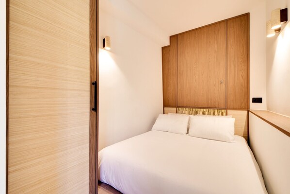 A bedroom with a bed, wooden wardrobe, and wall-mounted lighting.