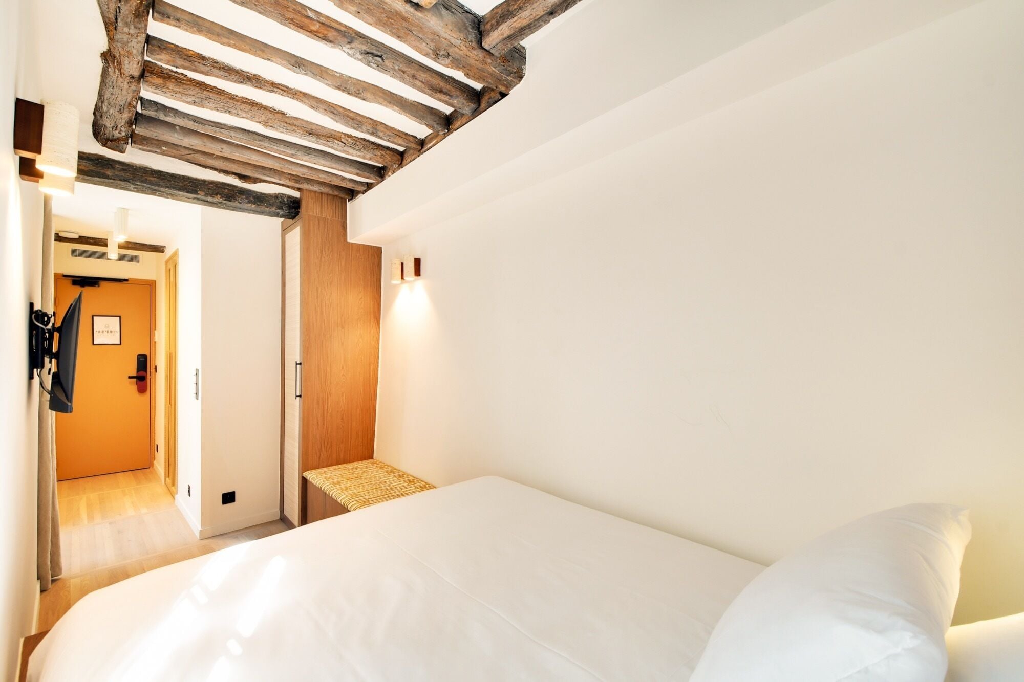 Un dormitorio con una cama, techo de madera, una lámpara fijada a la pared y una puerta con un letrero.