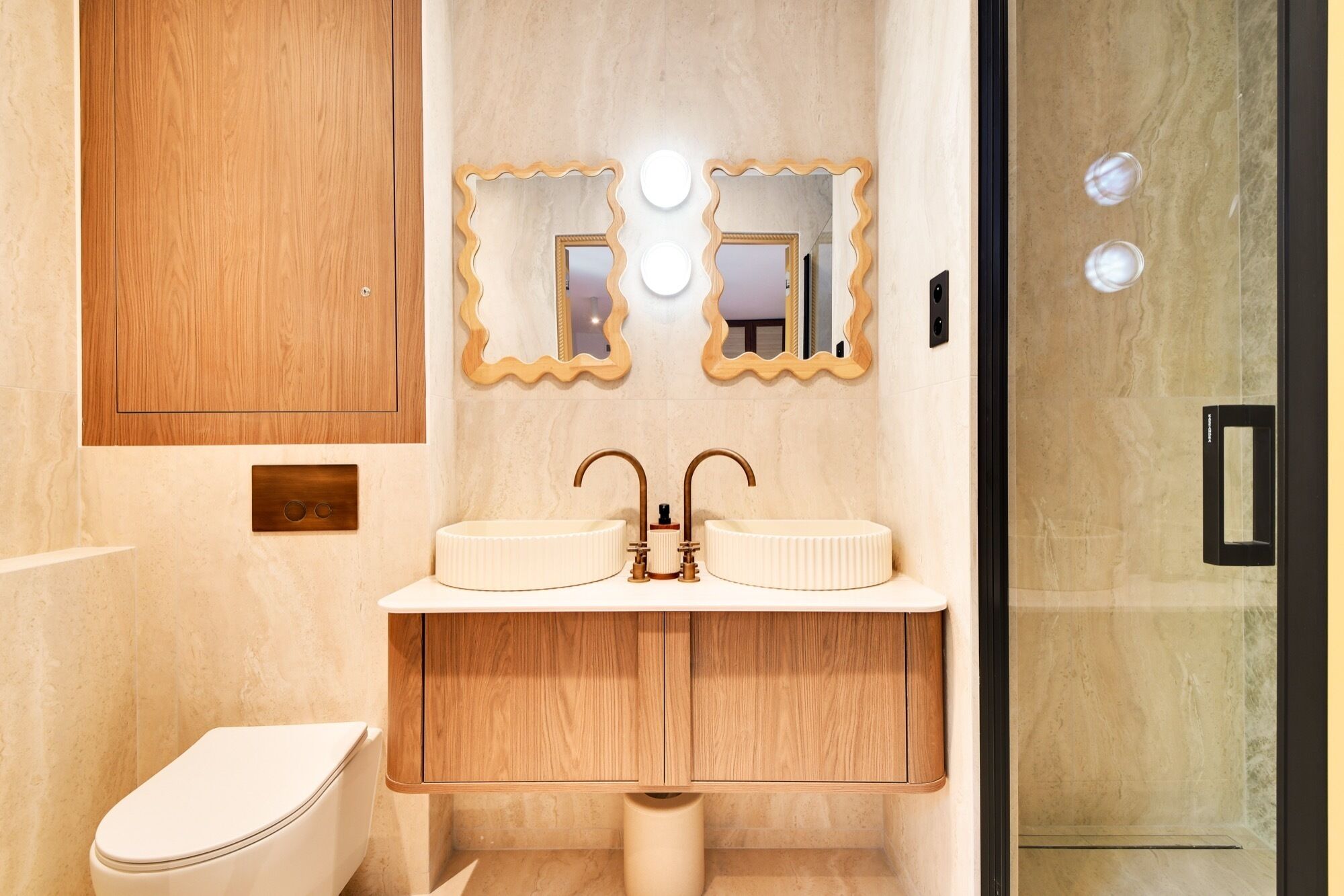A modern bathroom with a wooden vanity, two sinks, and a toilet.