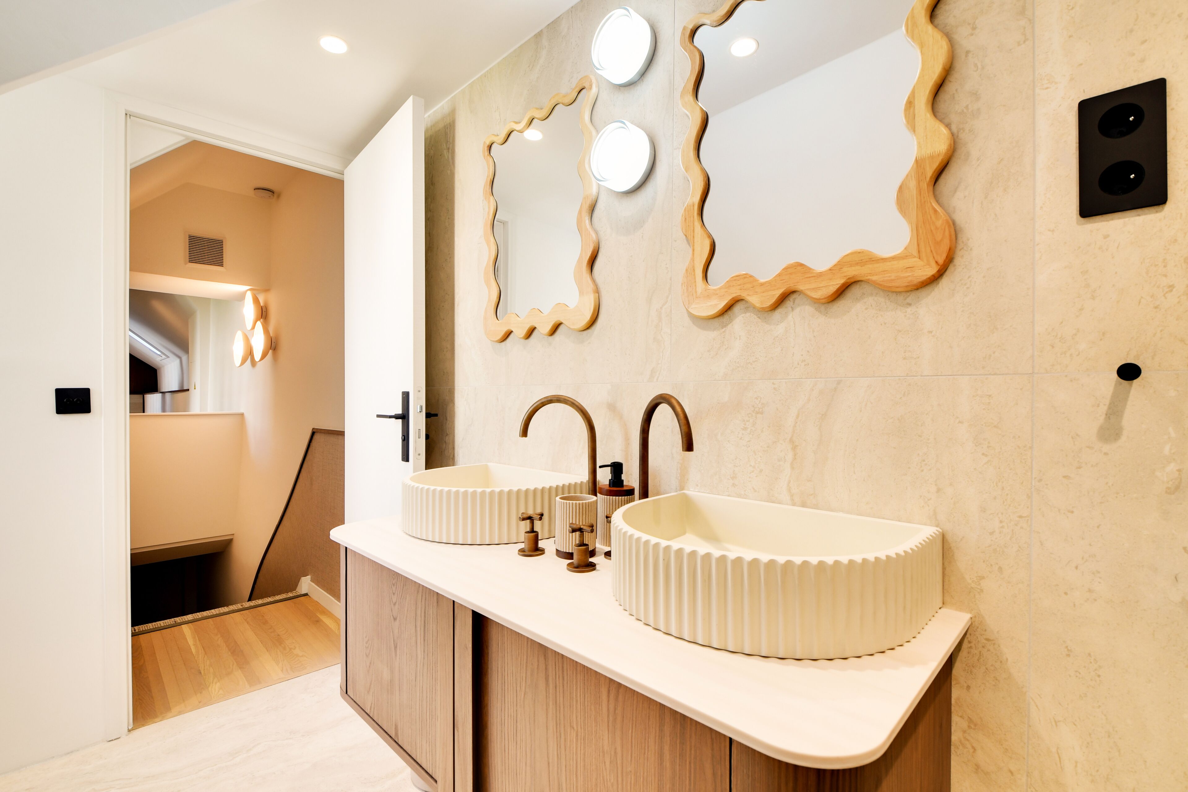 Un baño moderno con dos lavamanos, un armario de madera y tres espejos colgantes.