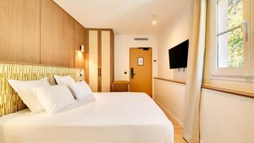 Habitación de hotel con una cama grande, paneles de madera en las paredes, un televisor montado y una ventana con cortinas.