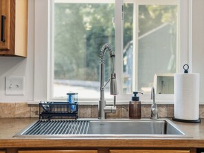 Eine Küche mit einer Spüle aus Edelstahl, einem Fenster mit Blick auf Grünflächen und einer Küchenpapierrolle.