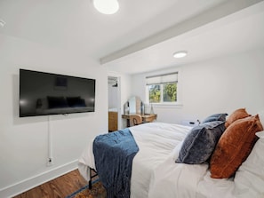 A bedroom with a bed, a television mounted on the wall, a window, and a desk with a chair. - The Hartson  Vintage Charm on the Ben Burr Trail (Spokane)