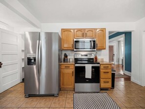 A kitchen with stainless steel appliances, wooden cabinets, and a tiled floor. - The Hartson  Vintage Charm on the Ben Burr Trail (Spokane)