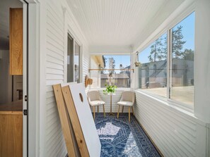 Une pièce aux murs recouverts de panneaux blancs, avec une grande fenêtre, une porte en bois et un tapis bleu à motifs.